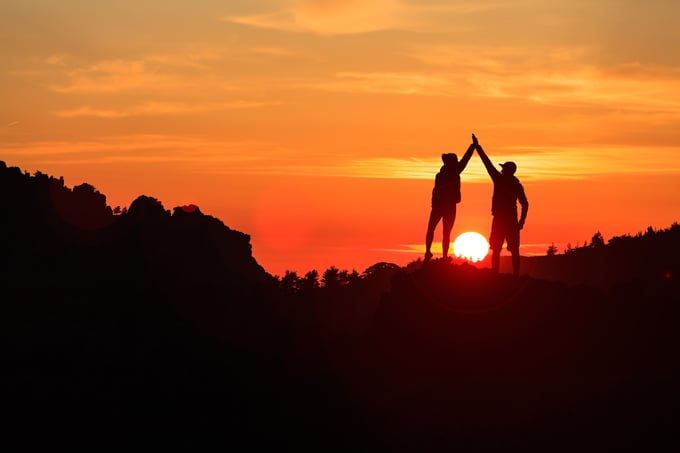 Two people high fiving in front of a sunset